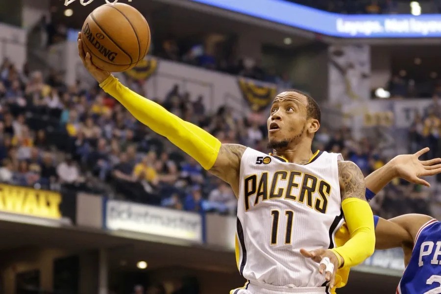Indiana Pacers player #11 shoots a basketball in an indoor arena during a game with spectators. Indiana Pacers player #11 shoots a basketball in an indoor arena during a game with spectators.
