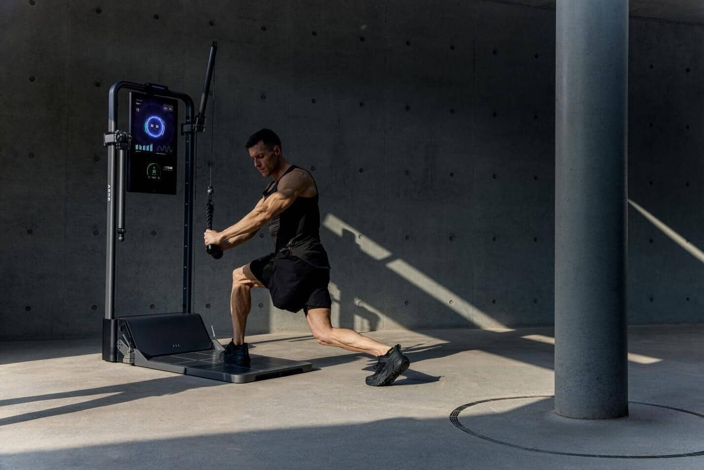 Man pulls rope on cable fitness machine in concrete-walled room.