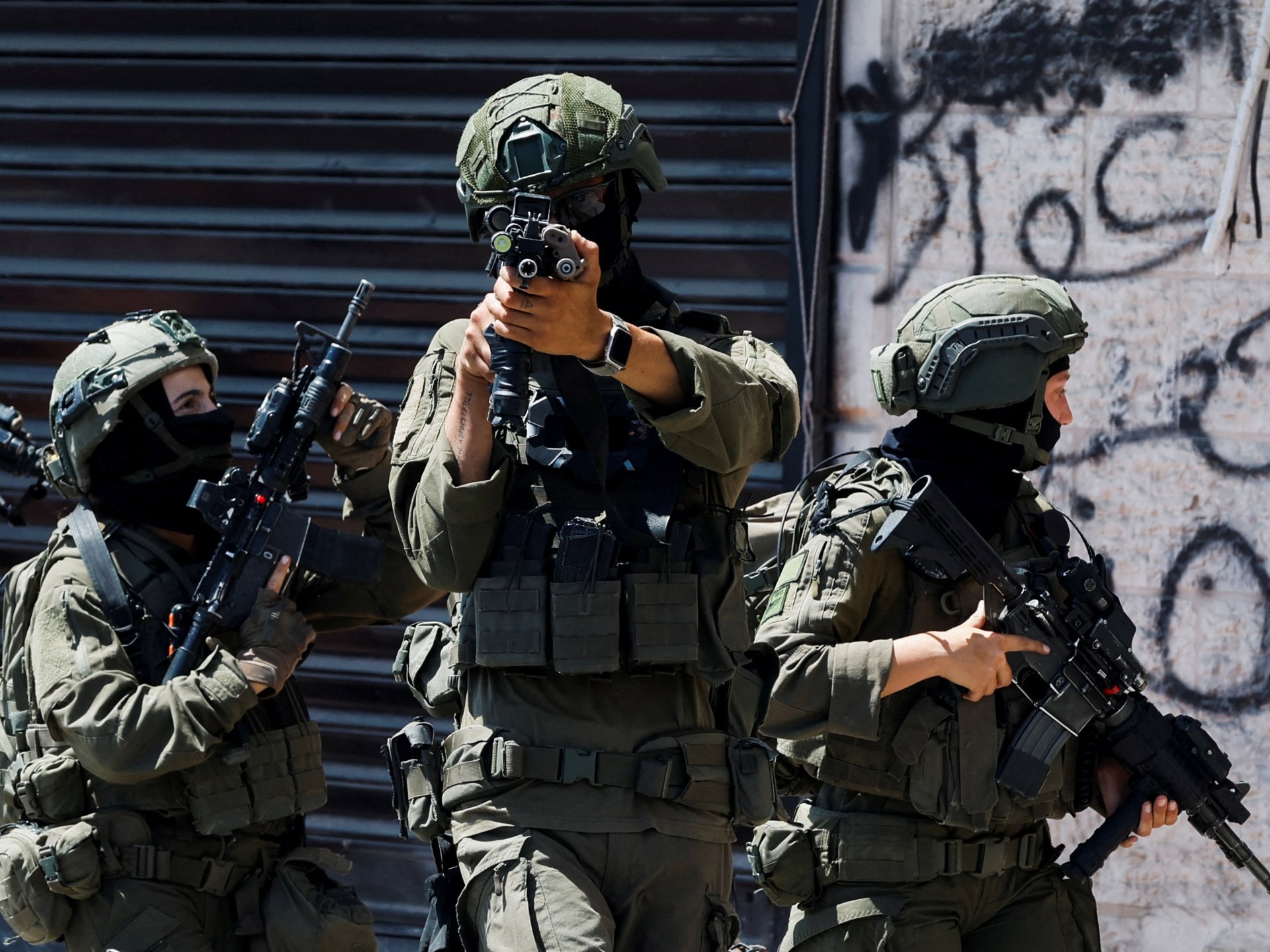 Three armed soldiers in tactical gear hold rifles near a graffiti-covered urban wall. Three armed soldiers in tactical gear hold rifles near a graffiti-covered urban wall.