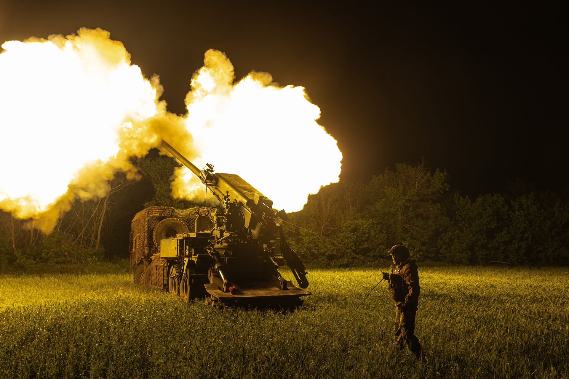 Soldier operates artillery gun in grassy field at night during firing. Soldier operates artillery gun in grassy field at night during firing.