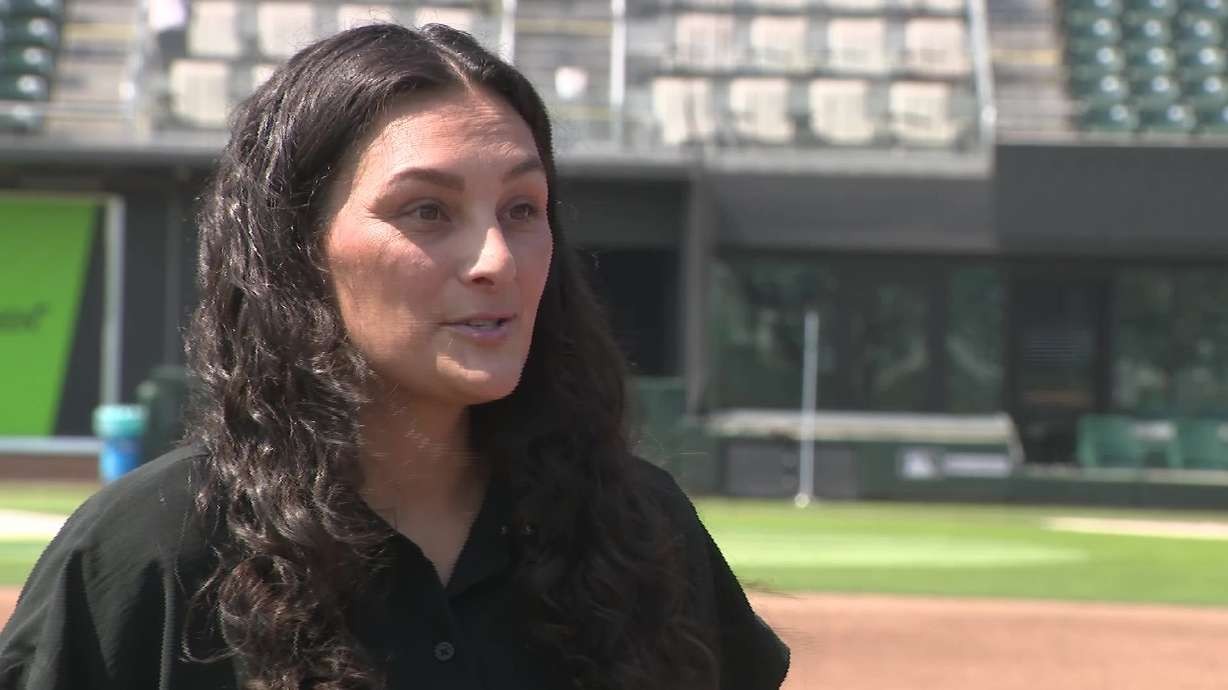 Long-haired woman in black shirt stands on baseball field with stadium seats visible. Long-haired woman in black shirt stands on baseball field with stadium seats visible.