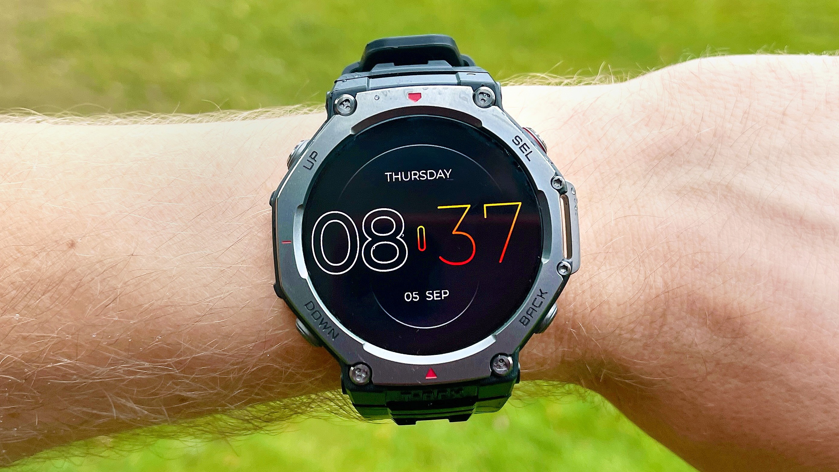 A smartwatch on a wrist displays Thursday 08:37 and 05 SEP against green grass.