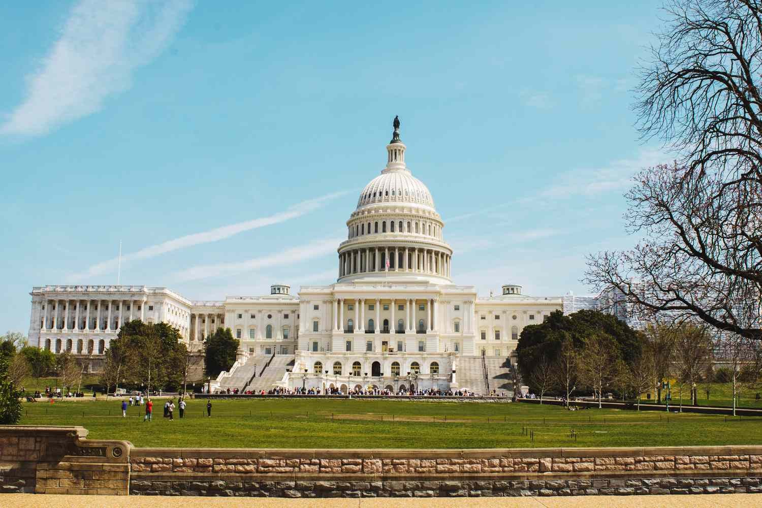U.S. Capitol building in Washington D.C. with people gathered on its lawn under clear sky. U.S. Capitol building in Washington D.C. with people gathered on its lawn under clear sky.