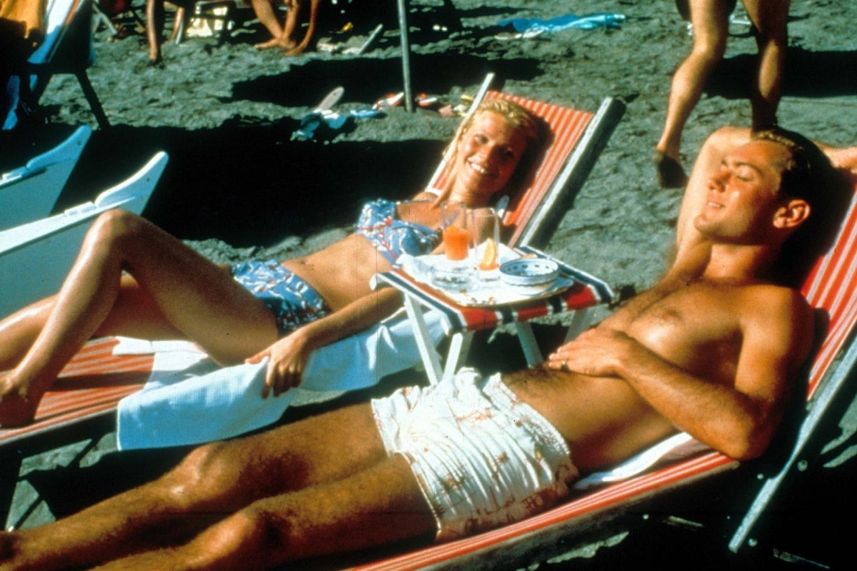 A man and woman sunbathe on striped beach chairs at a sandy beach. A man and woman sunbathe on striped beach chairs at a sandy beach.