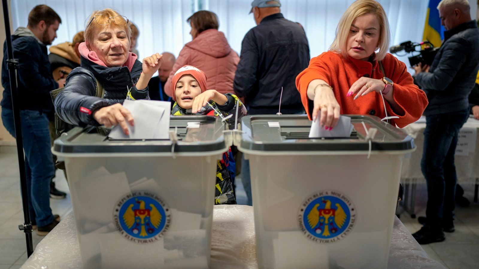 Voters cast ballots into transparent containers at a polling station during an election.