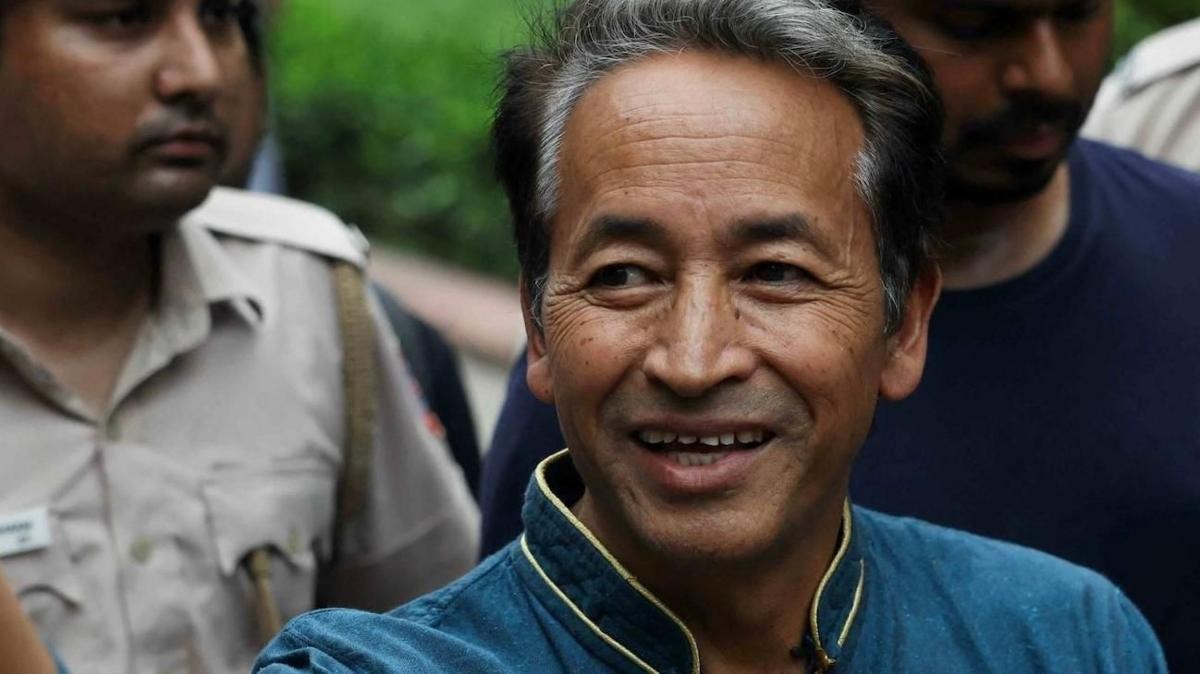 A middle-aged man in a blue shirt with yellow trim smiles outdoors among other people. A middle-aged man in a blue shirt with yellow trim smiles outdoors among other people.
