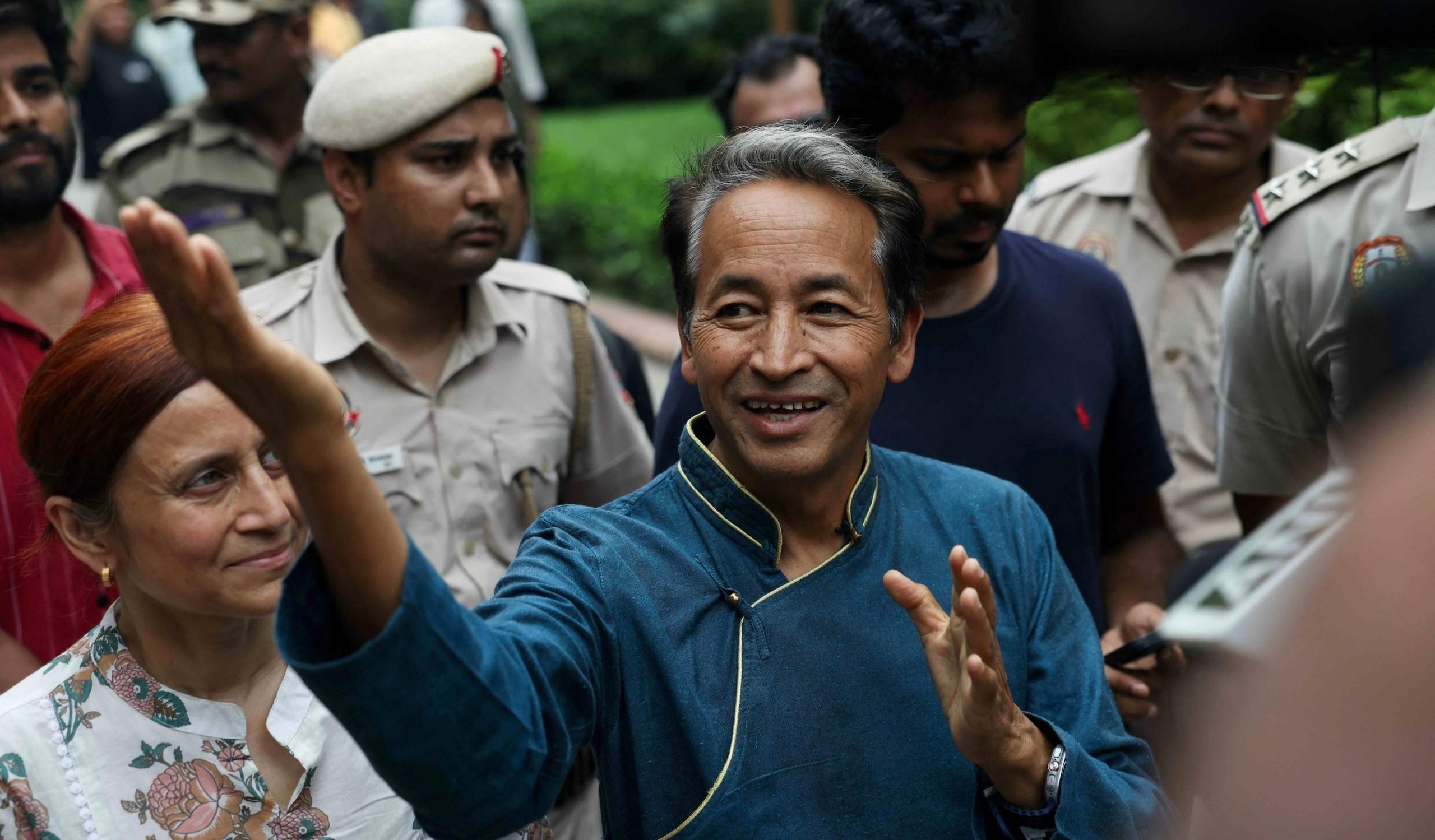 A middle-aged man in a blue shirt with yellow trim smiles outdoors among other people. A middle-aged man in a blue shirt with yellow trim smiles outdoors among other people.
