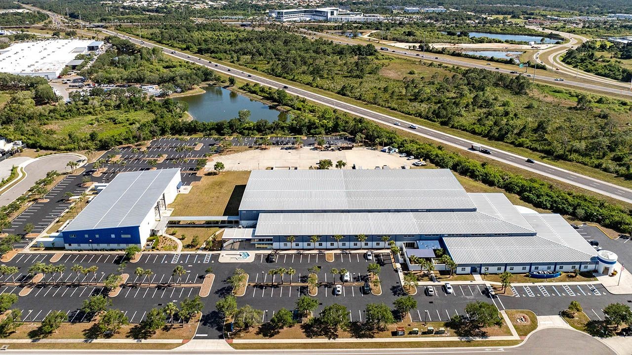 Aerial view shows large industrial building complex in suburban area near highway and lake. Aerial view shows large industrial building complex in suburban area near highway and lake.