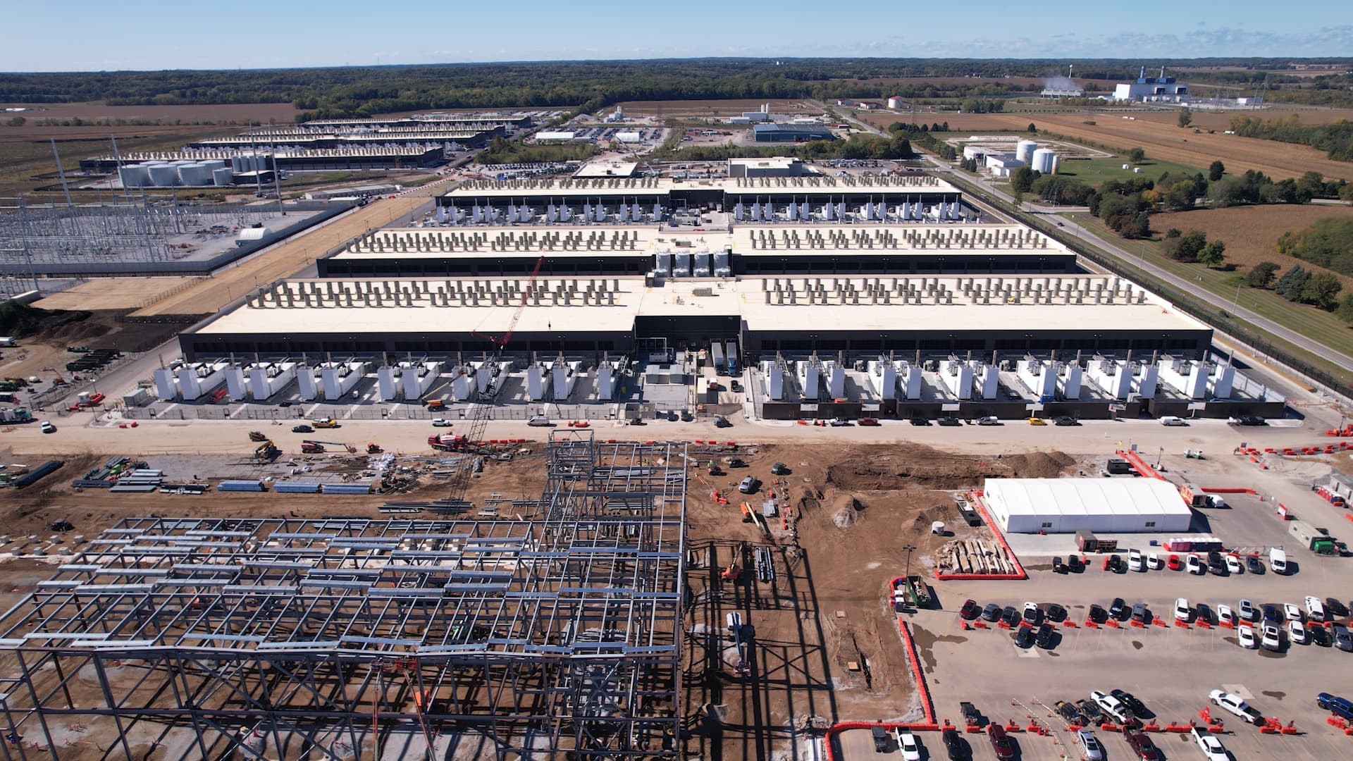 Industrial facility under construction in rural area with parking, cranes, and surrounding fields. Industrial facility under construction in rural area with parking, cranes, and surrounding fields.