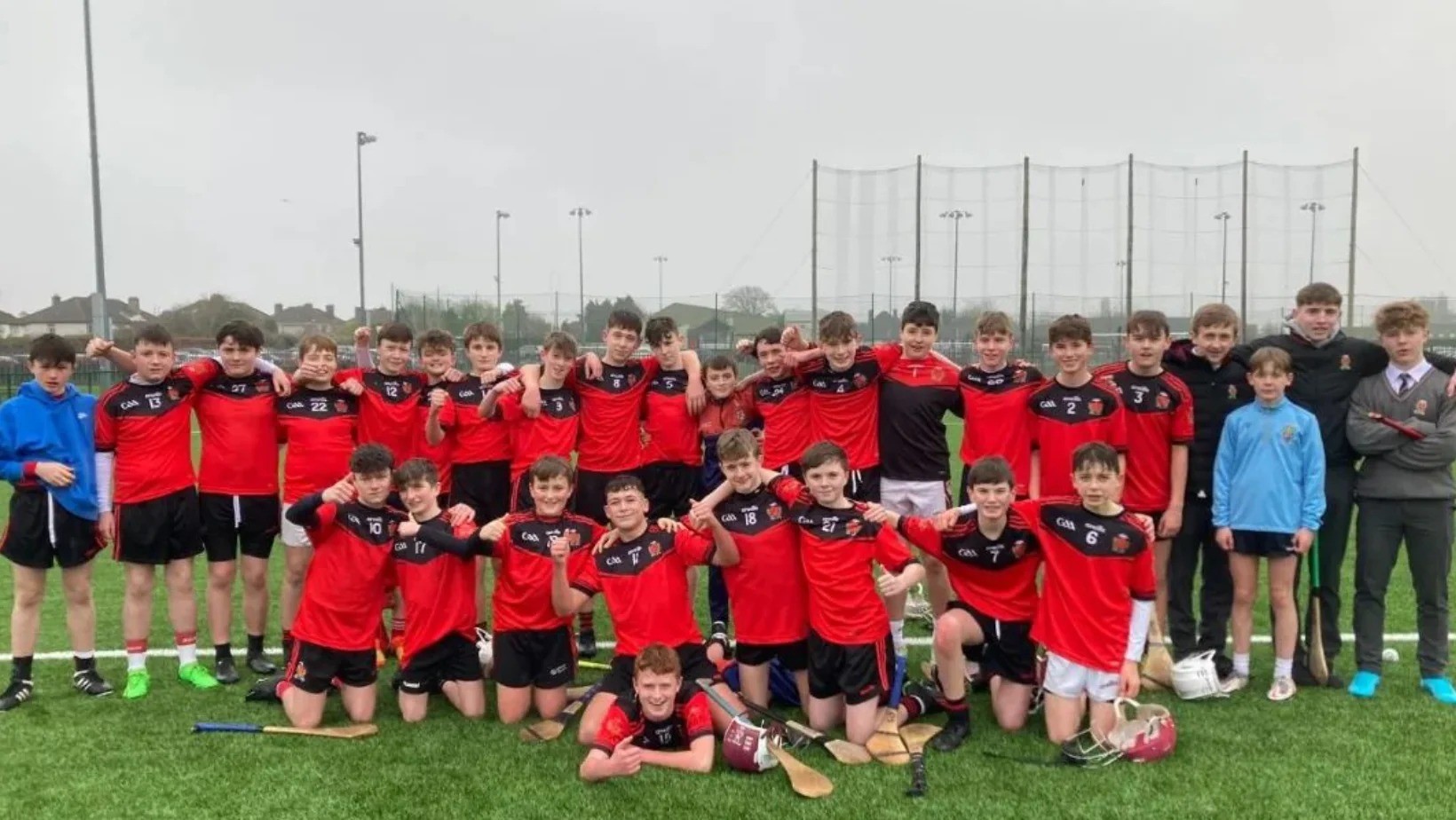 Youth sports team in red uniforms poses for a photo on a grass field with netting and hockey equipment. Youth sports team in red uniforms poses for a photo on a grass field with netting and hockey equipment.
