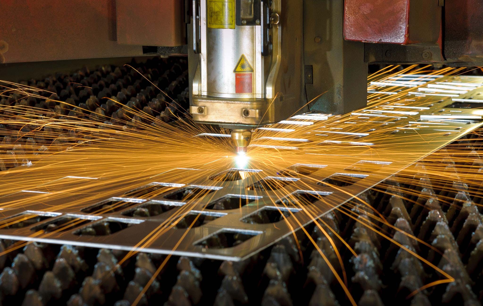 Industrial laser cutter emits bright orange sparks while cutting a metal sheet. Industrial laser cutter emits bright orange sparks while cutting a metal sheet.