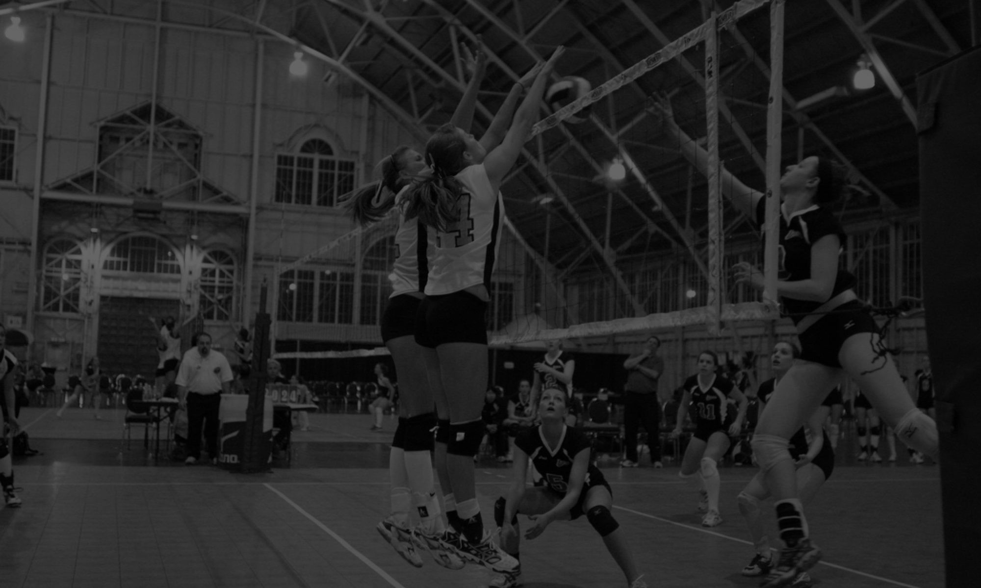 Volleyball players spike and block during an indoor gymnasium match.
