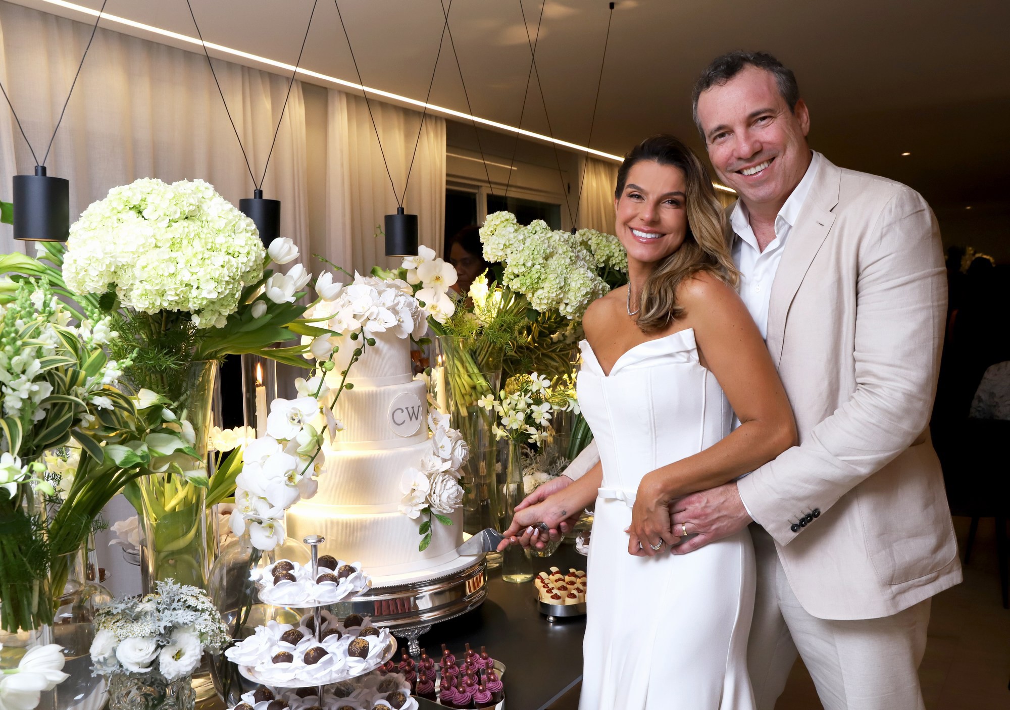 Bride and groom cut wedding cake at reception with floral arrangements. Bride and groom cut wedding cake at reception with floral arrangements.