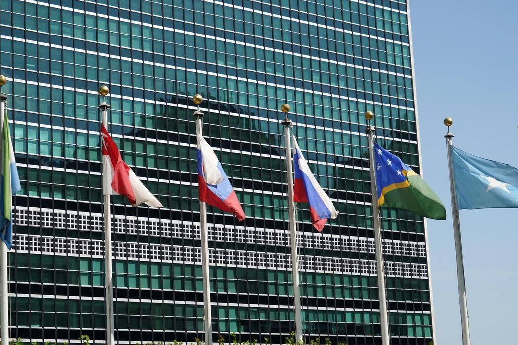 Multiple national flags wave before a tall modern glass office building. Multiple national flags wave before a tall modern glass office building.