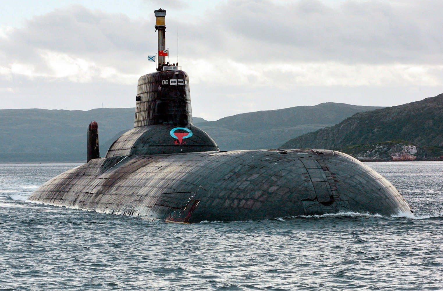 A submarine surfaces in choppy sea near mountainous coastline, creating wake. A submarine surfaces in choppy sea near mountainous coastline, creating wake.