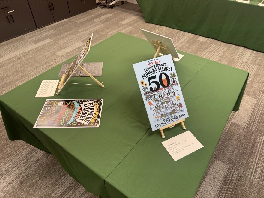 Three Larimer County Farmers' Market posters displayed on a gray surface show different designs. Three Larimer County Farmers' Market posters displayed on a gray surface show different designs.