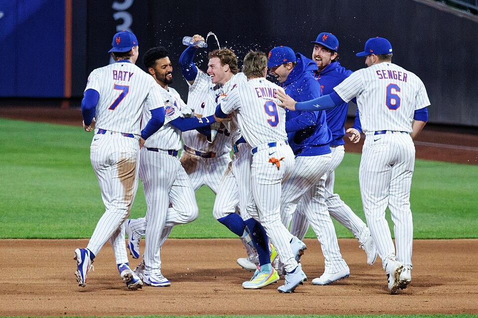 New York Mets players celebrate on a baseball field by spraying water and embracing. New York Mets players celebrate on a baseball field by spraying water and embracing.