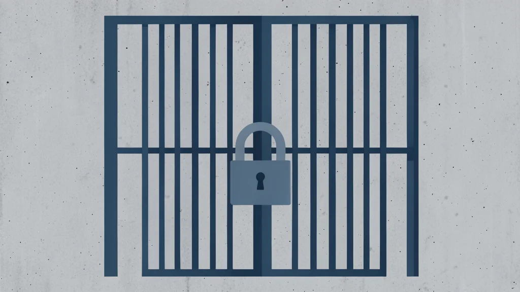 A heavy iron prison gate with vertical bars and a padlock, set against a plain concrete wall.