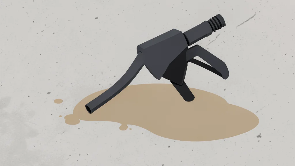 A fuel pump nozzle resting on a concrete surface next to a puddle of spilled liquid