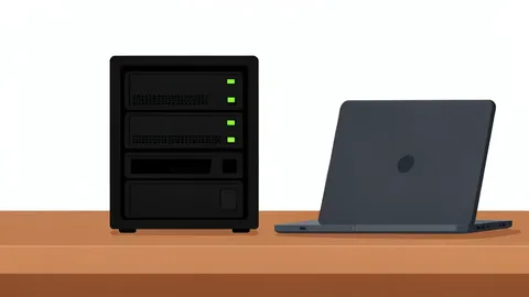 A small black server rack unit with blinking status lights on a wooden desk next to a laptop
