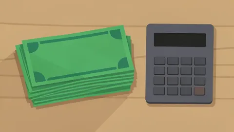 A stack of physical currency bills resting on a wooden desk next to a calculator
