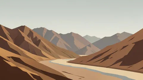 A rugged, arid mountain range bordering a dry riverbed under a hazy sky