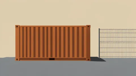 A wooden shipping container sits on a gravel lot near a border fence.