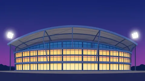 A modern stadium exterior with a curved roof and glass walls illuminated by floodlights against a twilight sky.