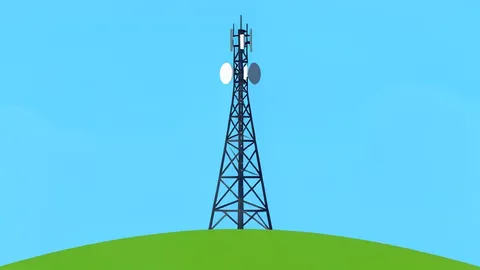 A modern telecommunications antenna tower standing on a grassy hill against a clear sky.