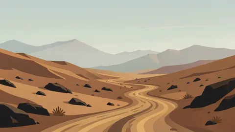 A rugged, arid landscape with winding dirt roads and distant mountain ranges under a hazy sky