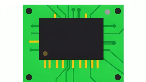 A close-up of a black rectangular computer memory chip with gold contact pins along the bottom edge, resting on a green circuit board.