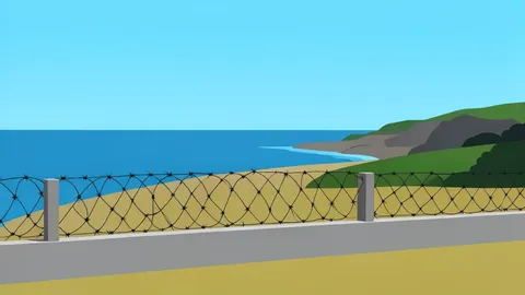A concrete border fence with barbed wire separating a coastal landscape from the sea