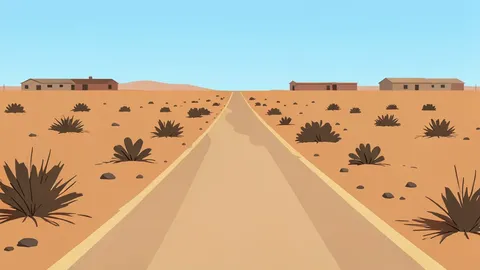 A dusty, unpaved road stretching through a dry, arid landscape with sparse vegetation and distant, low-rise buildings.