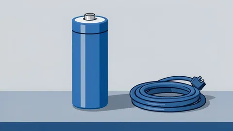 A cylindrical battery cell standing upright on a metal workbench next to a coiled charging cable