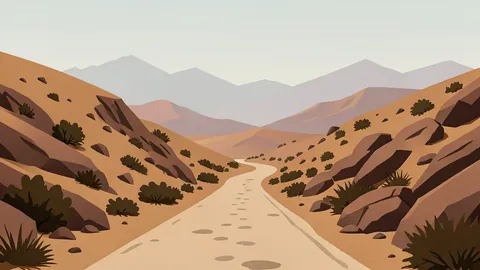 A dusty, unpaved road winding through arid, rocky highlands with sparse vegetation and distant mountain ridges under a hazy sky.